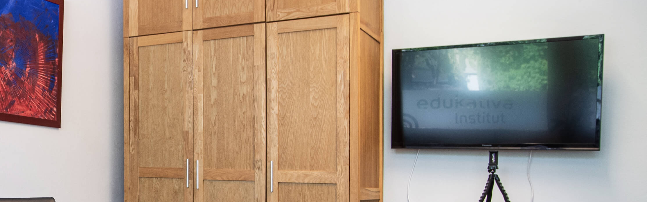 Ein gemütlicher Besprechungsraum mit Holztisch, Stühlen, einem Schrank und einem Fernseher an der Wand.