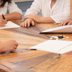 Mehrere Personen sitzen an einem Holztisch und besprechen die Antragstellung mit Unterlagen und Notizen.