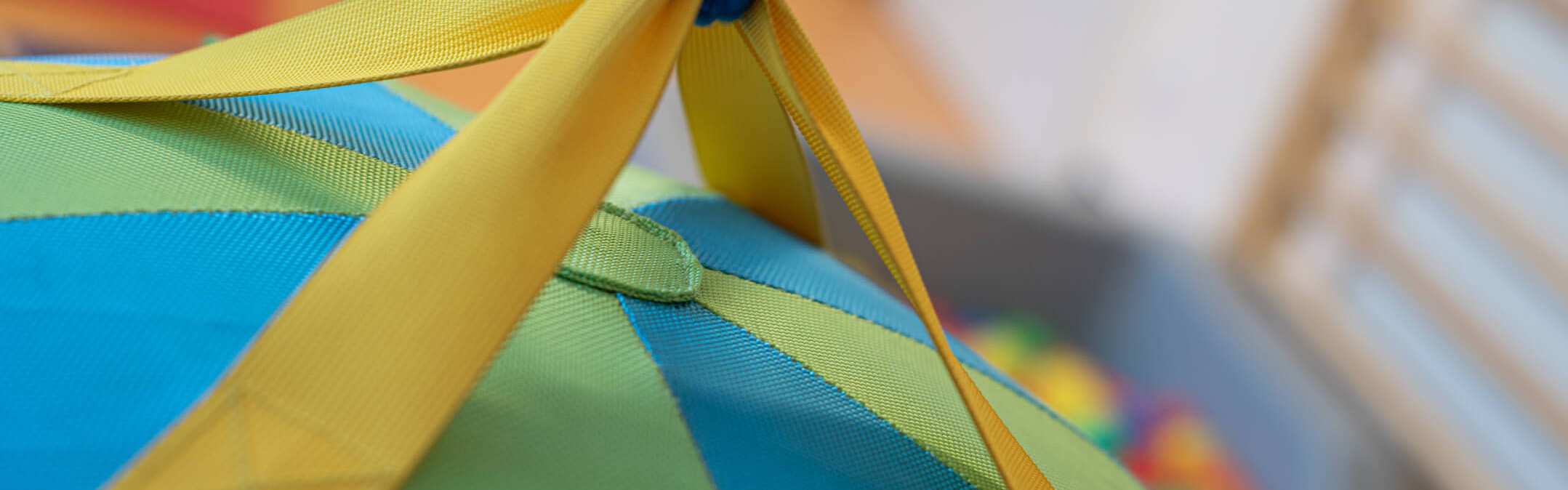 Ein bunter, hängender Therapieschaukelsitz mit gelbem Gurtband und blauem Seil in einem Spielzimmer.