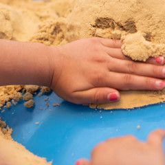 Kinderhände formen sanft Sand auf einer blauen Oberfläche, was an kreative Kunsttherapie erinnert.