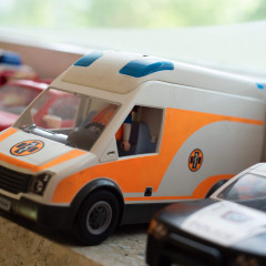 Spielzeugautos, darunter ein orange-weißes Krankenwagenmodell, stehen nebeneinander auf einer Fensterbank in einer Kita.