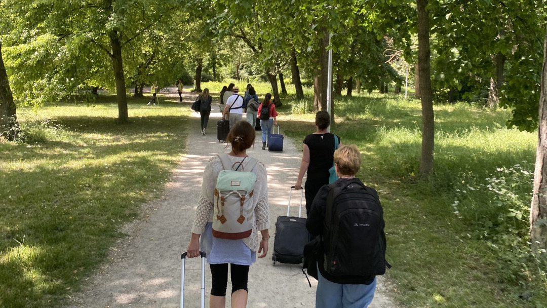 Personen ziehen Koffer auf einem sonnigen Waldweg, während sie sich auf Ferien 2023 vorbereiten.