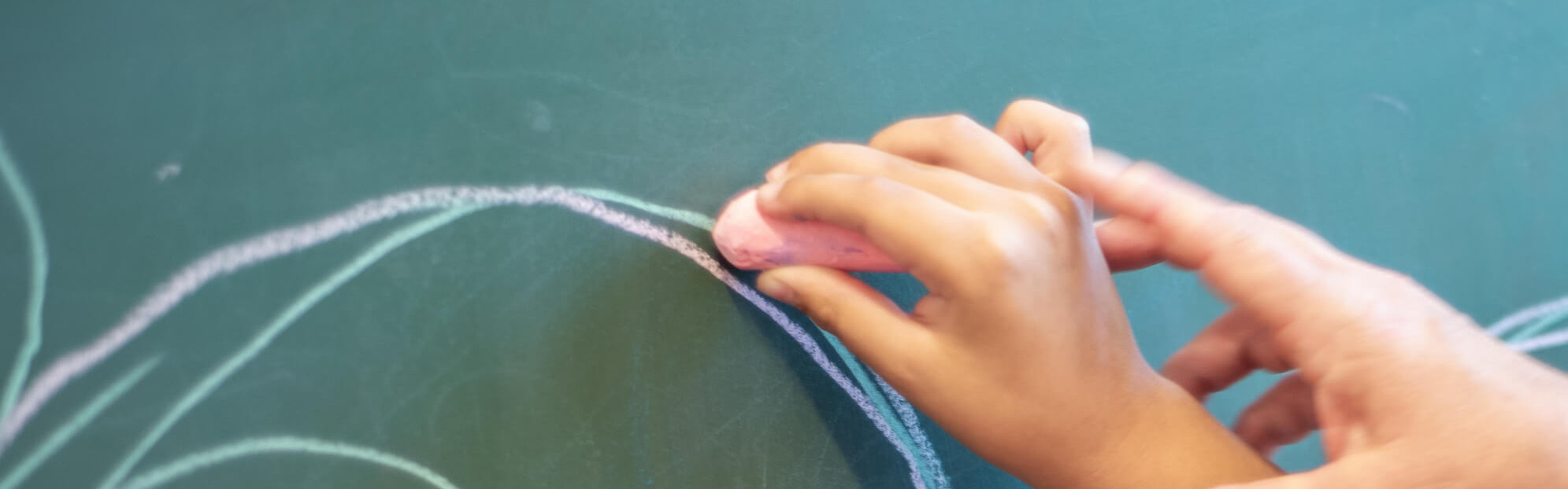 Eine Hand hilft einem Kind, mit Kreide auf einer Tafel zu zeichnen, was auf eine unterstützende Lerntherapie hinweist.