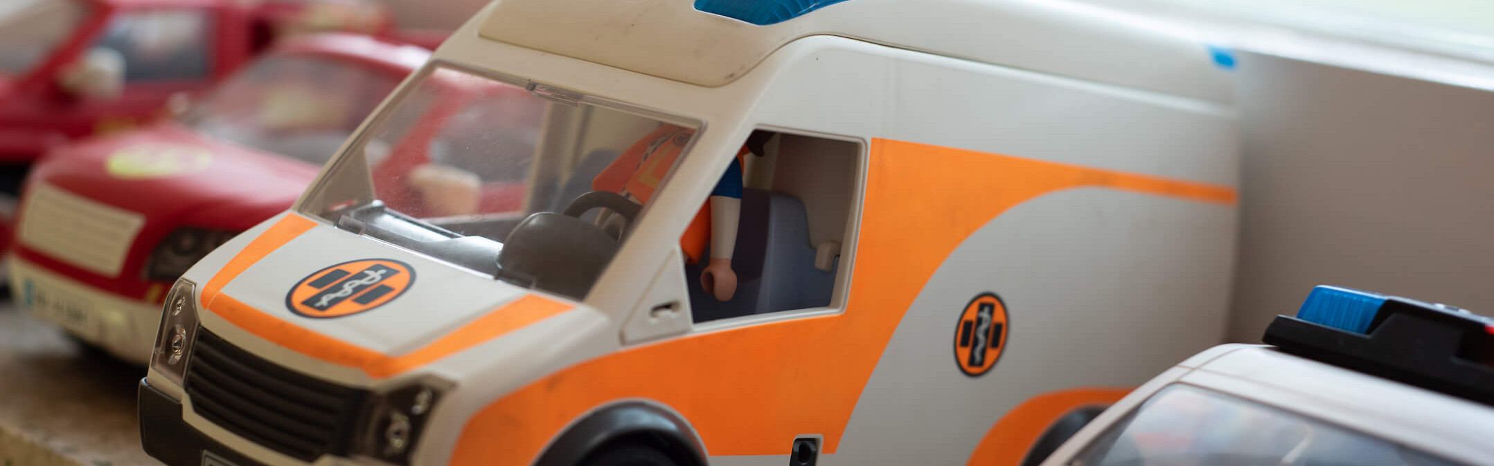 Spielzeugautos, darunter ein orange-weißes Krankenwagenmodell, stehen nebeneinander auf einer Fensterbank in einer Kita.
