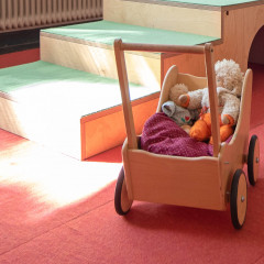 Ein Holzspielzeugwagen mit Kuscheltieren steht auf einem roten Teppich vor einer kleinen Holzrampe, ideal für Spieltherapie.