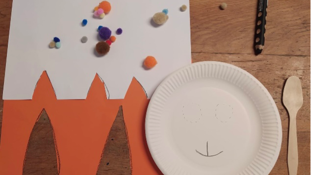 Bastelmaterialien für ein Osterhasenprojekt liegen auf einem Tisch, mit bunten Pompons und einem bemalten Pappteller.