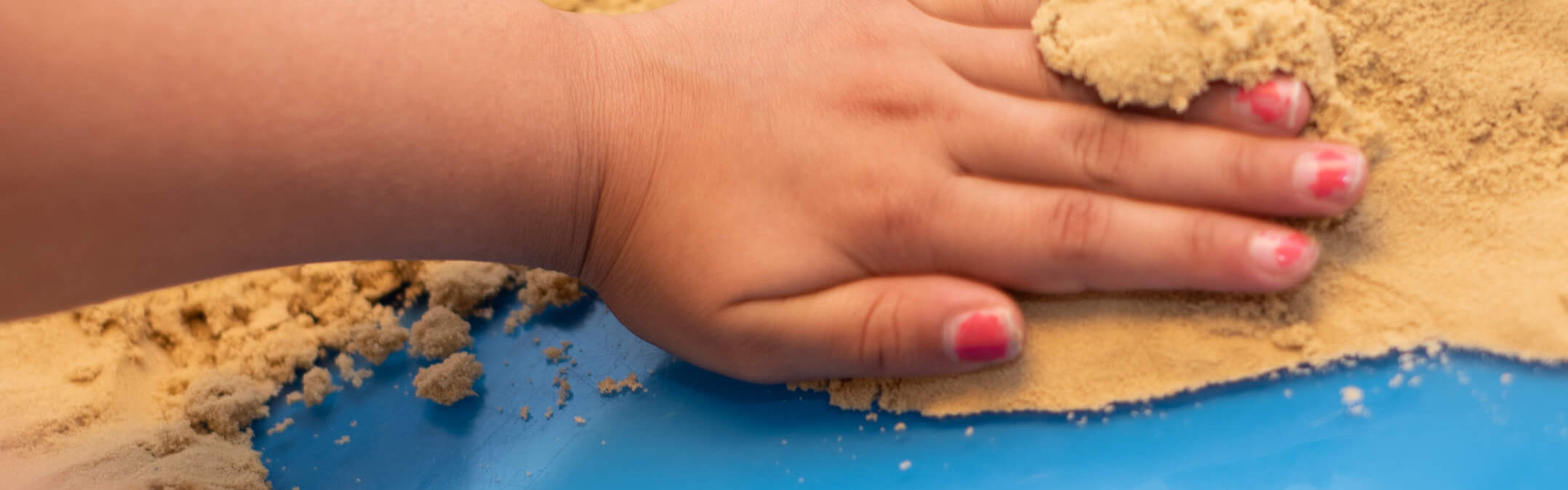 Kinderhände formen sanft Sand auf einer blauen Oberfläche, was an kreative Kunsttherapie erinnert.