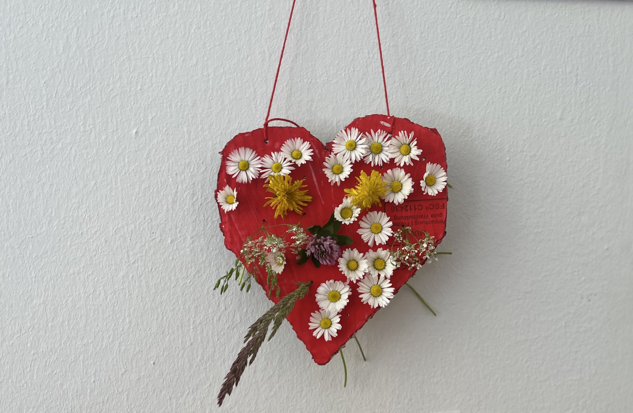 Ein rotes Herz aus Pappe, dekoriert mit bunten Blumen, hängt an einer Wand und verleiht der Umgebung eine frische Note.